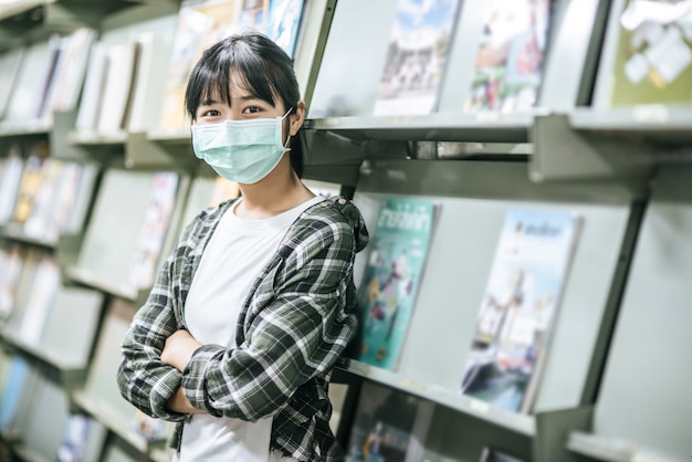 Uma mulher usando uma máscara e procurando livros na biblioteca.