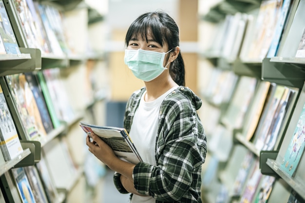 Uma mulher usando uma máscara e procurando livros na biblioteca.