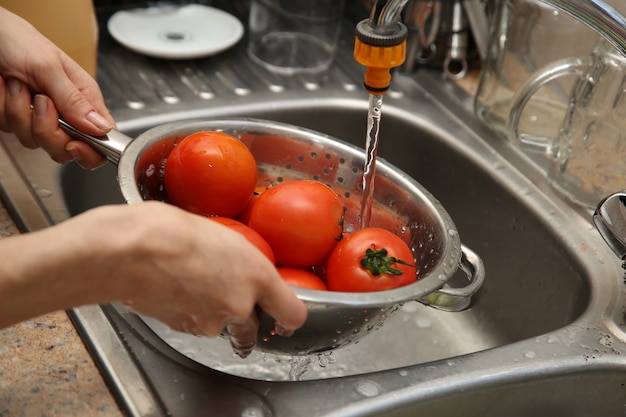 Uma mulher usando uma peneira e uma pia de cozinha para lavar tomates.