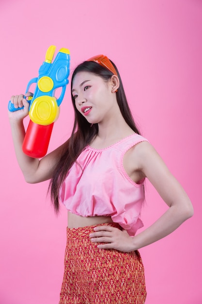 Uma mulher vestiu-se em uma roupa popular tailandesa tradicional que guardara uma arma de água em um fundo cor-de-rosa.