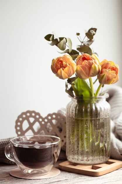 Uma natureza morta festiva com um arranjo de flores em um vaso e uma xícara de chá e coisas aconchegantes.