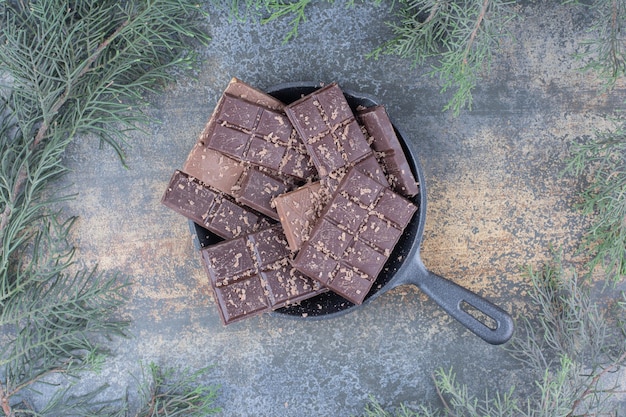 Uma panela escura cheia de chocolates fatiados em fundo de mármore. foto de alta qualidade