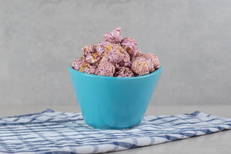 Foto grátis uma pequena tigela azul com pipoca roxa com sabor, colocada sobre um pano de prato na mesa de mármore.