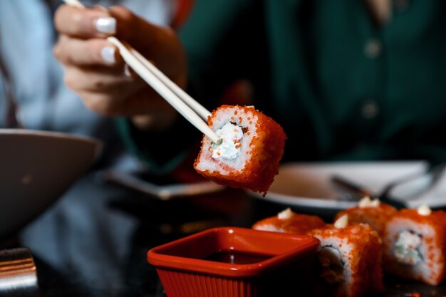 Uma pessoa mergulha em rolos de sushi de suace enquanto usa palitos