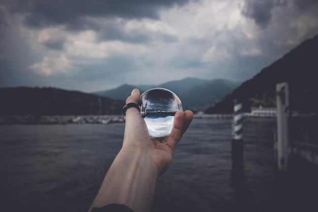 Uma pessoa segurando uma bola de cristal com o reflexo de montanhas altas e belas nuvens