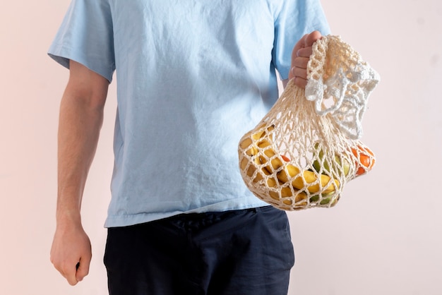 Uma pessoa segurando uma sacola de malha com frutas e vegetais frescos e crus, conversa ecológica e sem resíduos