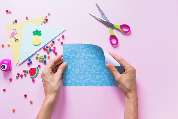 Uma pessoa transformando o papel de scrapbook azul com itens decorativos em fundo rosa
