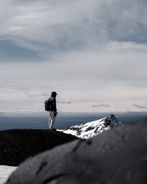 Uma pessoa usando mochila em pé no topo de uma montanha sob céu nublado