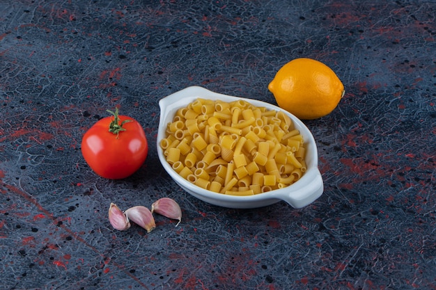 Uma placa branca de massa crua com tomates vermelhos frescos e limão em uma superfície escura.