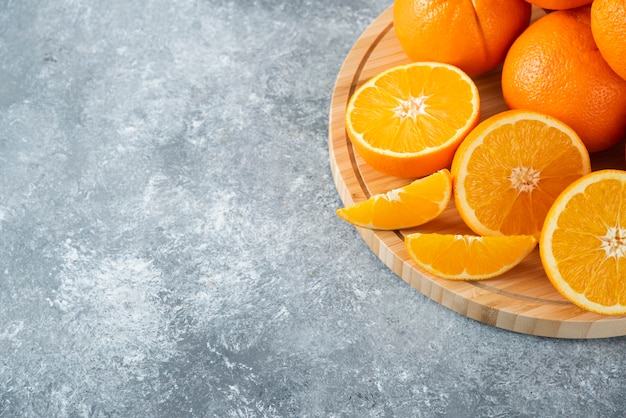 Uma placa de madeira cheia de suculentas fatias de fruta laranja na mesa de pedra.