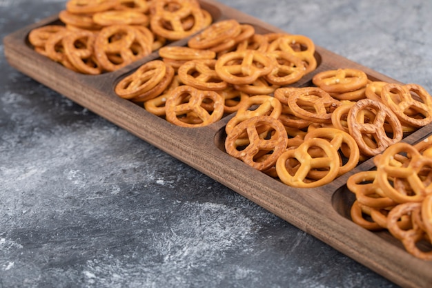 Uma placa de madeira com biscoitos salgados secos de pretzels colocada sobre uma superfície de pedra