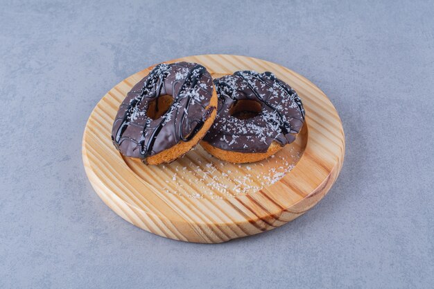 Uma placa de madeira com deliciosos donuts de chocolate com granulado.