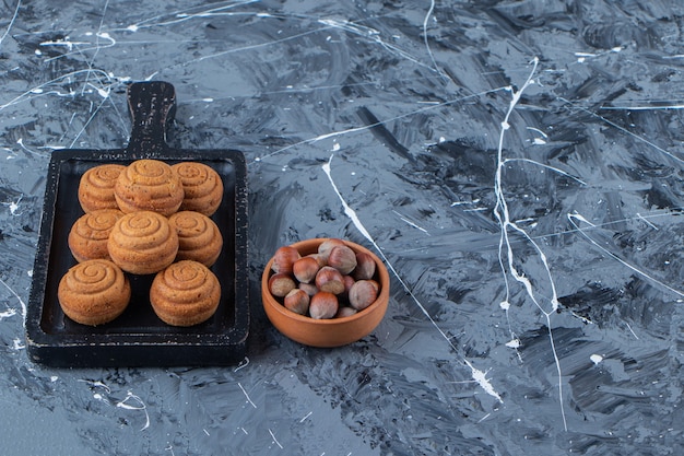 Uma placa de madeira preta de biscoitos doces redondos frescos para chá com nozes saudáveis em um fundo de mármore.
