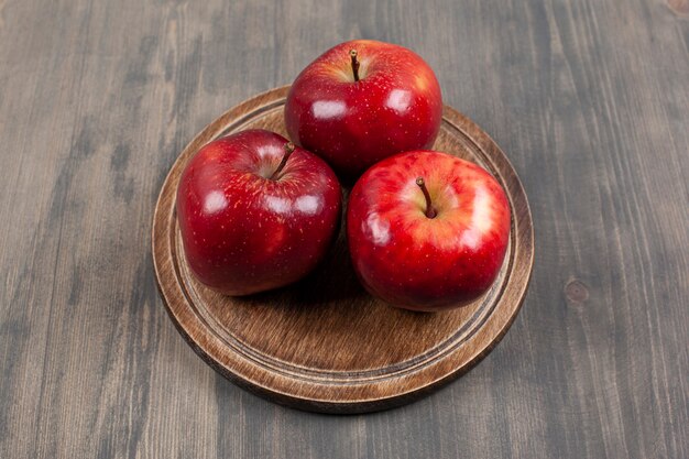 Uma placa marrom com maçãs vermelhas suculentas em uma mesa de madeira. Foto de alta qualidade