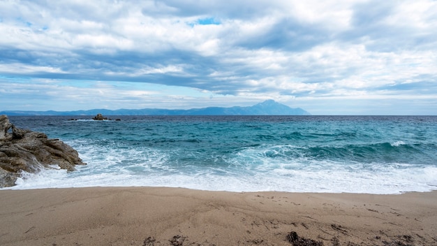 Uma praia com pedras e ondas azuis do mar Egeu, terra e montanha