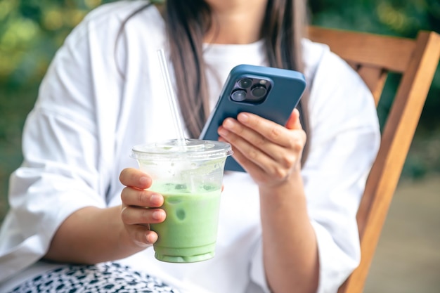 Foto grátis uma rapariga bebe um matcha latte e usa um smartphone.