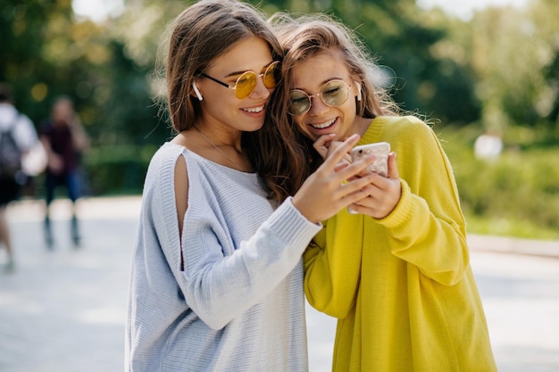 Uma senhora muito charmosa em óculos elegantes está segurando o smartphone e conversando com amigos em videochamada Garotas felizes passam tempo online com amigos