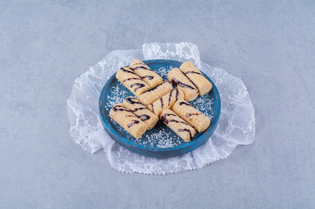 Uma tábua de madeira azul com palitos de doce com granulado e calda de chocolate.