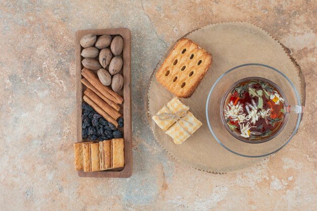 Uma tábua de madeira cheia de biscoitos doces e uma xícara de chá de ervas