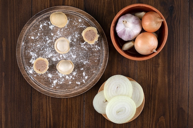 Foto grátis uma tábua de madeira com bolinhos pelmeni caseiros com uma tigela de barro com cebolas.