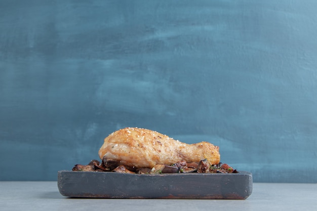 Uma tábua de madeira com carne de coxa de frango frito e berinjela.