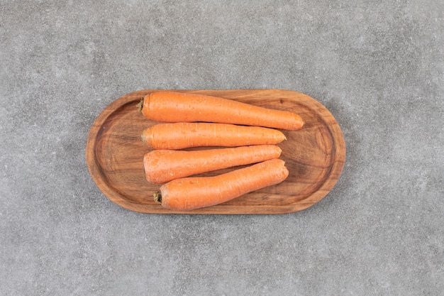 Uma tábua de madeira com cenouras doces frescas colocadas sobre uma superfície de pedra.