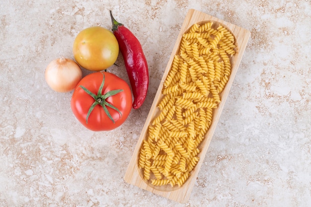 Foto grátis uma tábua de madeira com macarrão espiral cru e vegetais