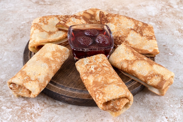 Uma tábua de madeira com saborosos crepes e geléia de morango