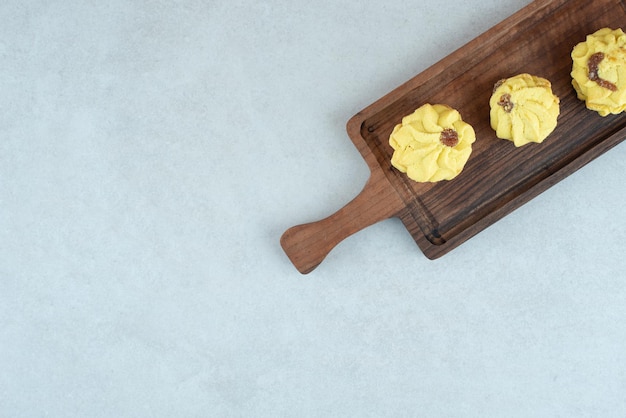 Uma tábua de madeira com três deliciosos biscoitos na mesa branca.