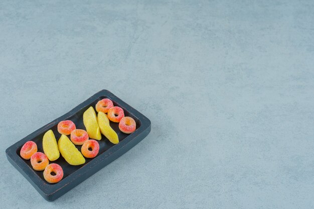 Foto grátis uma tábua de madeira preta com balas de mascar em forma de banana e balas redondas de gelatina de laranja em forma de anéis