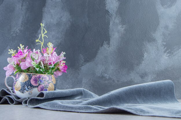 Uma taça de flores em um pedaço de tecido, na mesa branca.