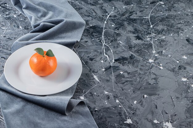Uma tangerina em um prato sobre um pedaço de tecido, na mesa mista.