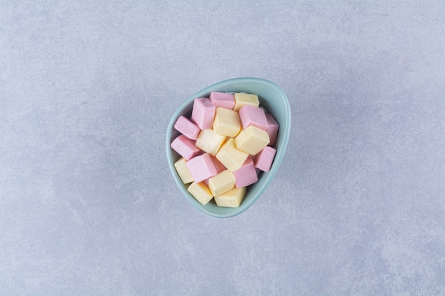 Uma tigela azul cheia de doces pastéis rosa e amarelos