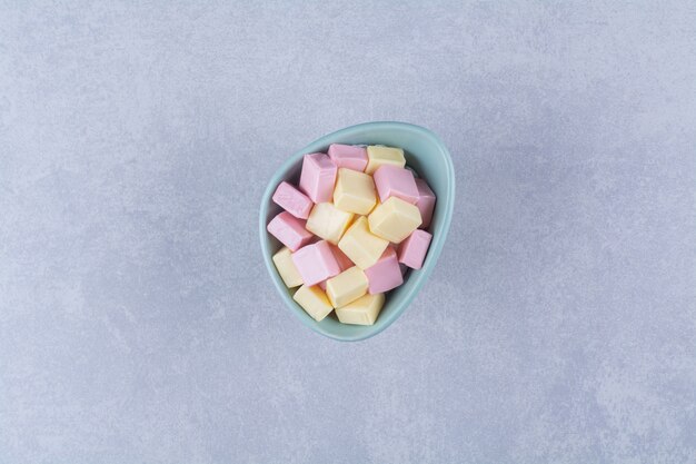 Uma tigela azul cheia de doces pastéis rosa e amarelos