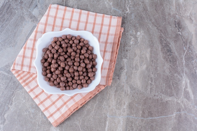 Uma tigela branca cheia de deliciosas bolas de milho de chocolate na toalha de mesa.