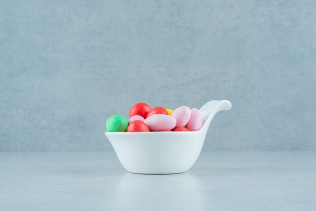 Uma tigela branca cheia de doces redondos doces coloridos em fundo branco. Foto de alta qualidade