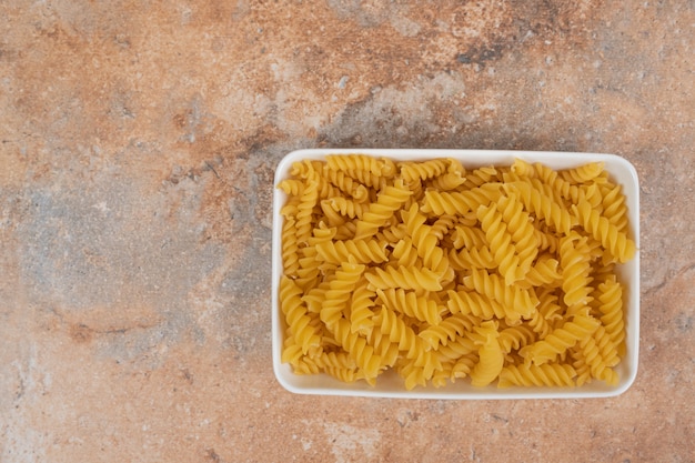 Foto grátis uma tigela branca de macarrão não preparado no fundo de mármore. foto de alta qualidade