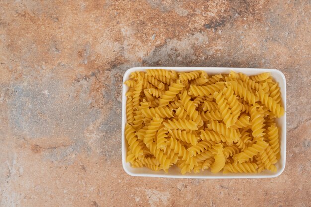 Uma tigela branca de macarrão não preparado no fundo de mármore. Foto de alta qualidade