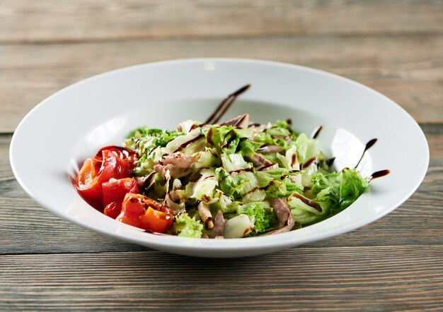 Uma tigela branca na mesa de madeira, servida com salada de legumes leve com frango, colorau e folhas de alface. Parece delicioso e saboroso.