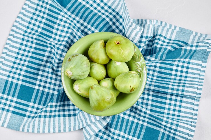 Foto grátis uma tigela de figos verdes com uma toalha de mesa azul em branco.