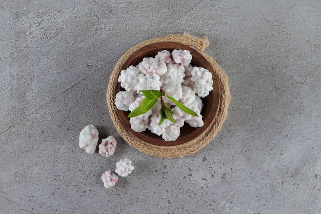 Uma tigela de madeira cheia de doces brancos doces com folhas de hortelã em uma mesa de pedra.