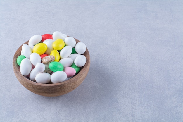 Uma tigela de madeira cheia de doces de feijão coloridos em fundo cinza. foto de alta qualidade