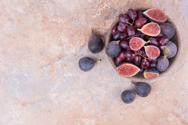 Uma tigela de madeira com bagas de cornel e figos roxos.