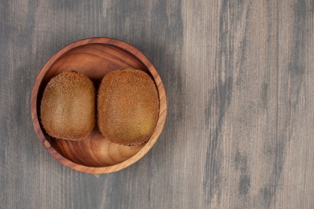 Foto grátis uma tigela de madeira com dois kiwis frescos em uma mesa de madeira. foto de alta qualidade