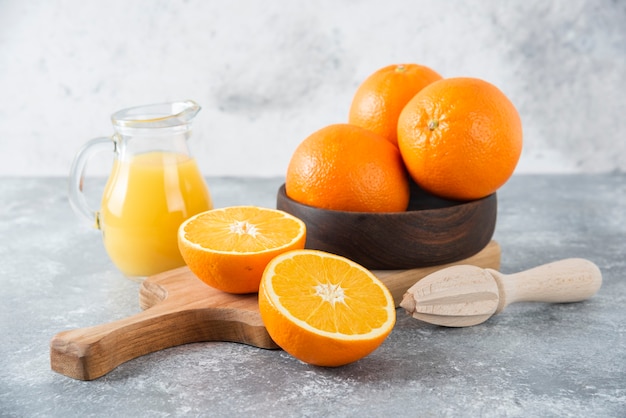 Uma tigela de madeira com frutas frescas de laranja e uma jarra de vidro com suco.