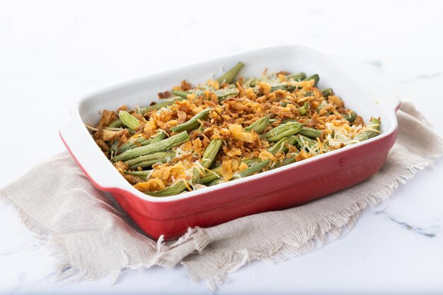 Uma tradicional caçarola de feijão verde coberta com cebolas fritas francesas e creme de cogumelo isolado em fundo branco.