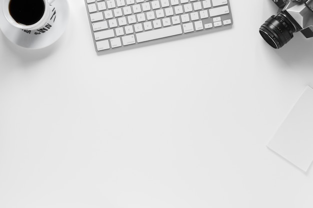 Uma visão aérea da xícara de café; teclado; câmera e papel em fundo branco
