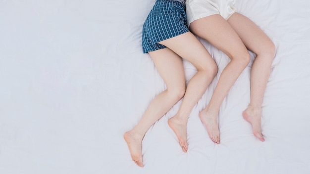 Uma visão aérea das pernas do casal de lésbicas na cama branca