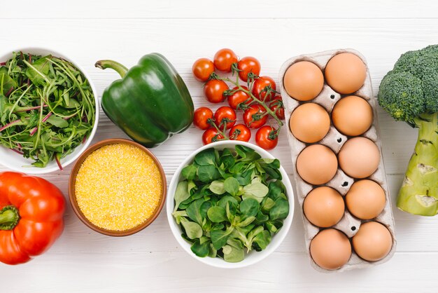Uma visão aérea de legumes frescos; ovos e polenta na mesa de madeira branca