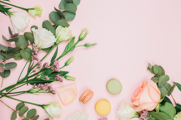 Uma visão aérea de macaroons com rosa fresca; limonium e eustoma flores sobre fundo rosa